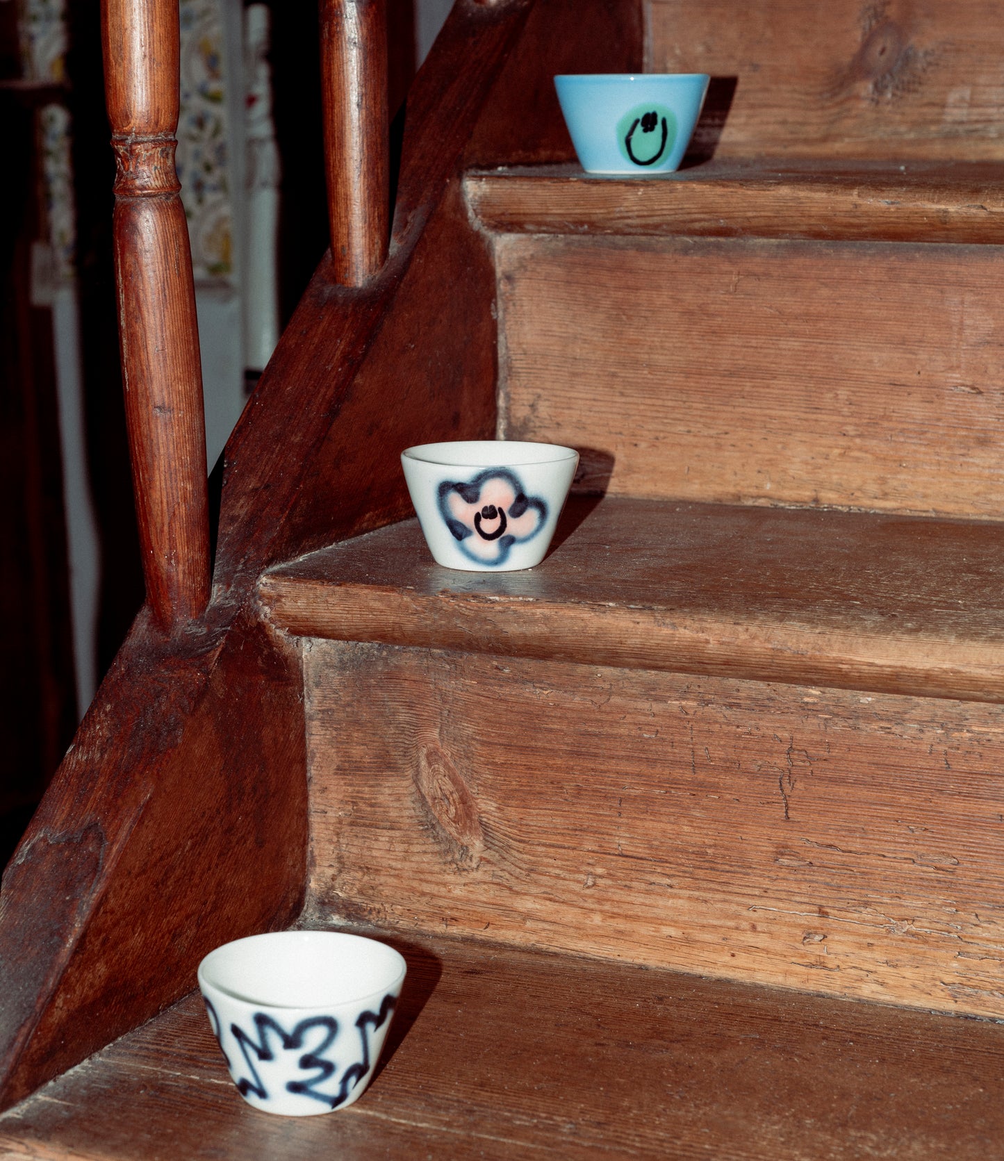 Three Super Cup Kawaii from Frizbee Ceramics placed on the steps of a vintage staircase.