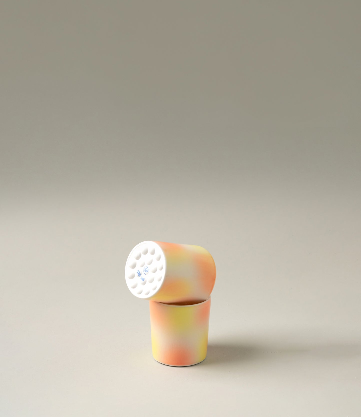 Bulle Cup from Frizbee Ceramics has a unique gradient painted pattern. The product has warm colors like orange, peach and yellow. The bottom of the cup looks like it's made of small bubbles.