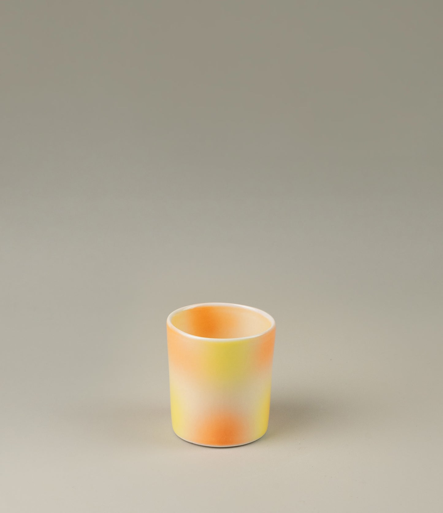 Bulle Cup from Frizbee Ceramics has a unique gradient painted pattern. The product has warm colors like orange, peach and yellow. The bottom of the cup looks like it's made of small bubbles.