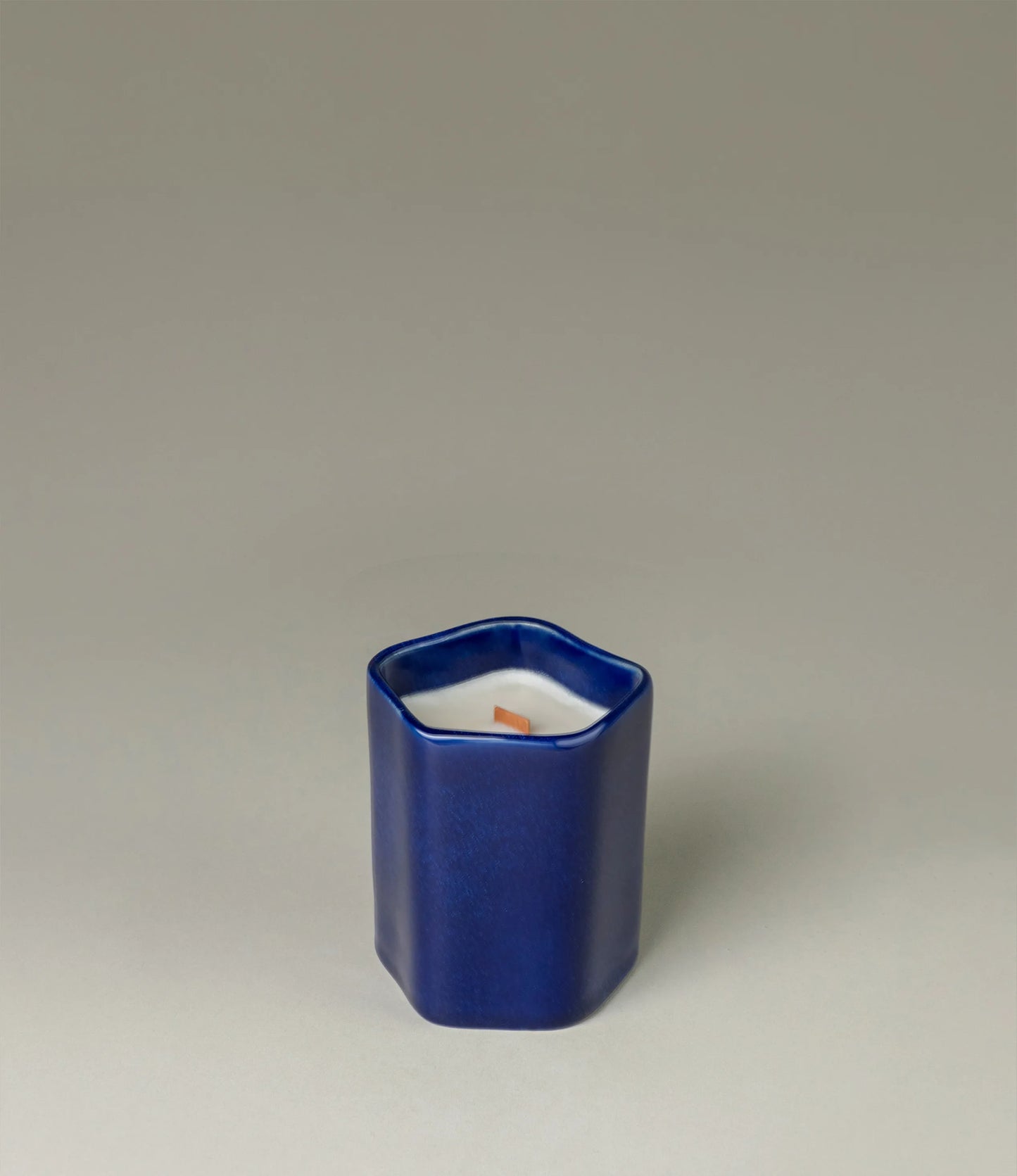 A scented Wax Candle designed by Ocactuu. The candle has an amber scent and it comes in a glossy dark blue ceramic. The material has a subtle spotted texture. The candle wick is made of wood for a more natural feeling.