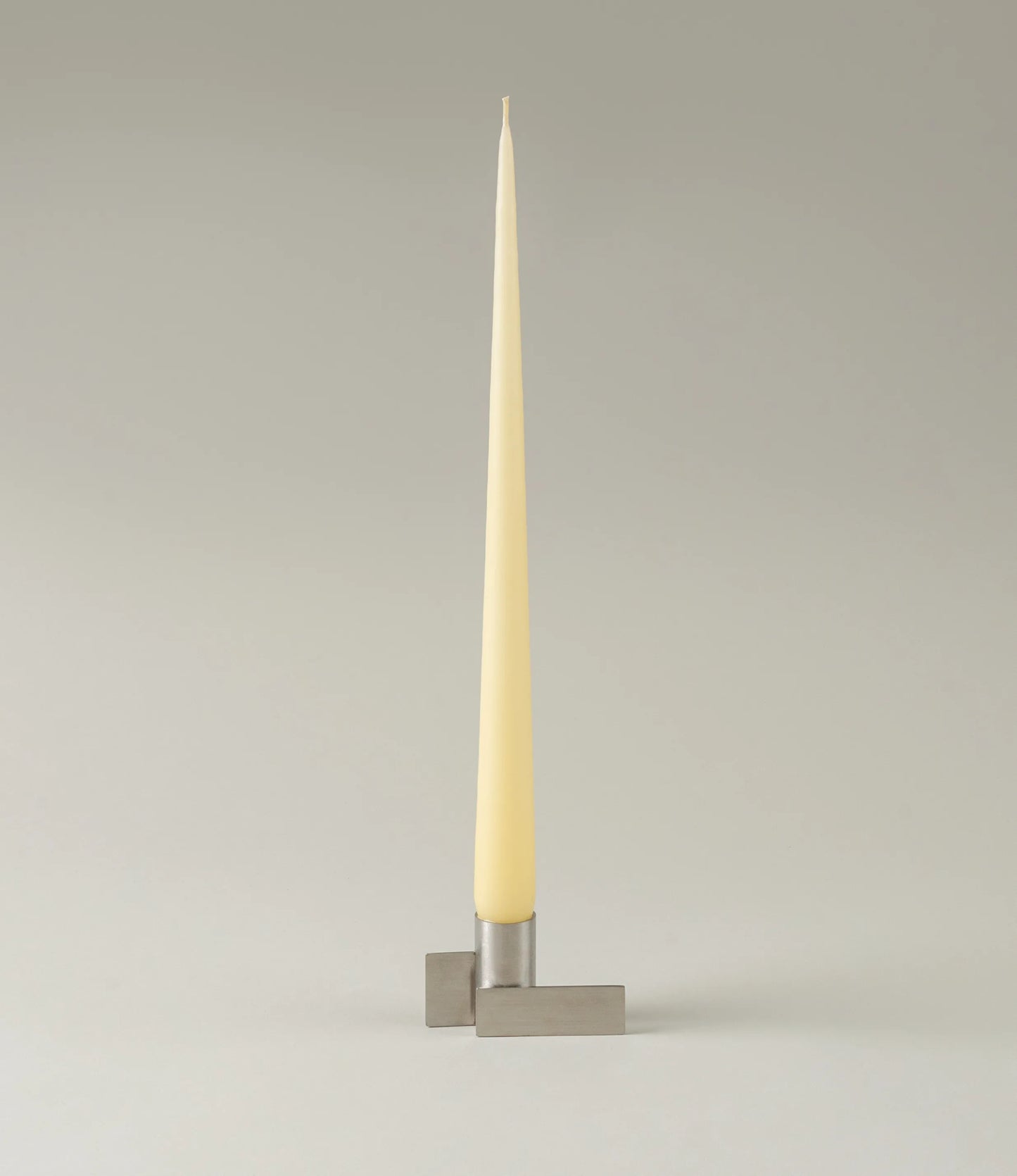 Ester&Erik Taper Candle coming in a Buttermilk shade. The product is showcased in a stainless steel Icon Candleholder from Stences.
