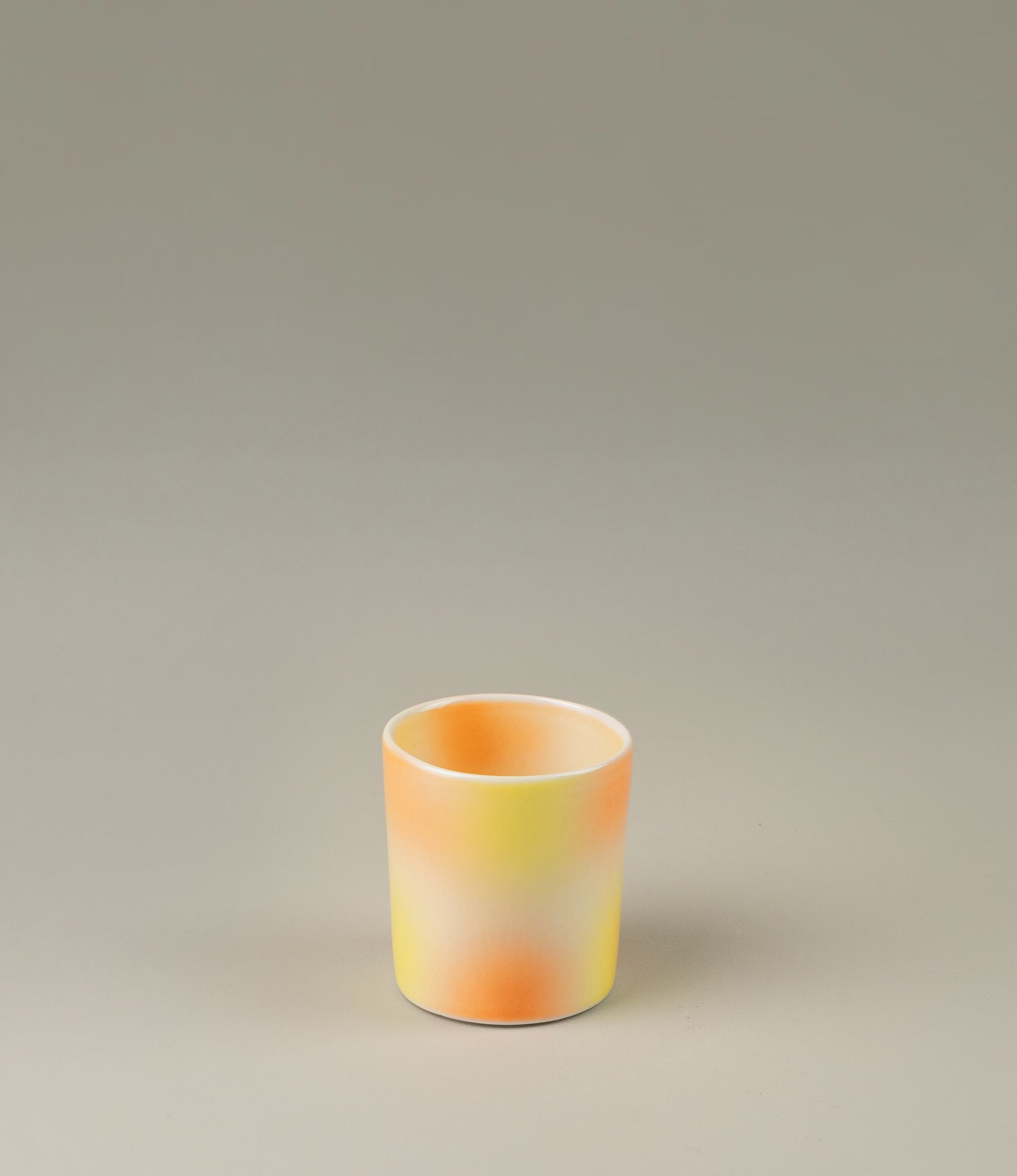 Bulle Cup from Frizbee Ceramics has a unique gradient painted pattern. The product has warm colors like orange, peach and yellow. The bottom of the cup looks like it's made of small bubbles.