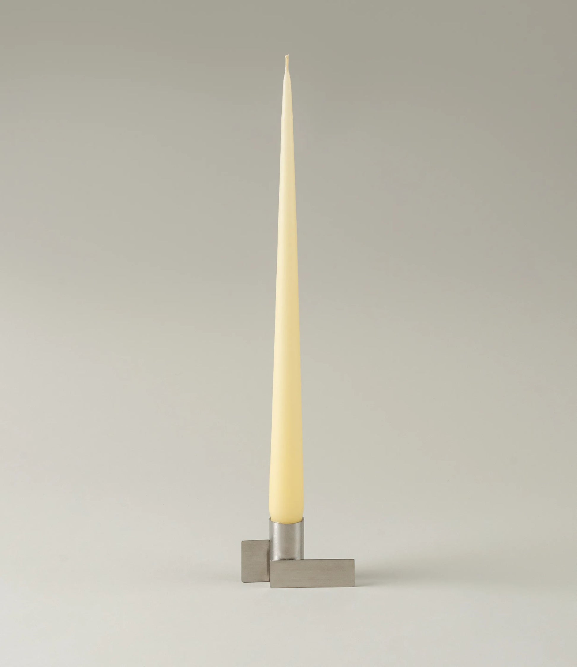 Ester&Erik Taper Candle coming in a Buttermilk shade. The product is showcased in a stainless steel Icon Candleholder from Stences.